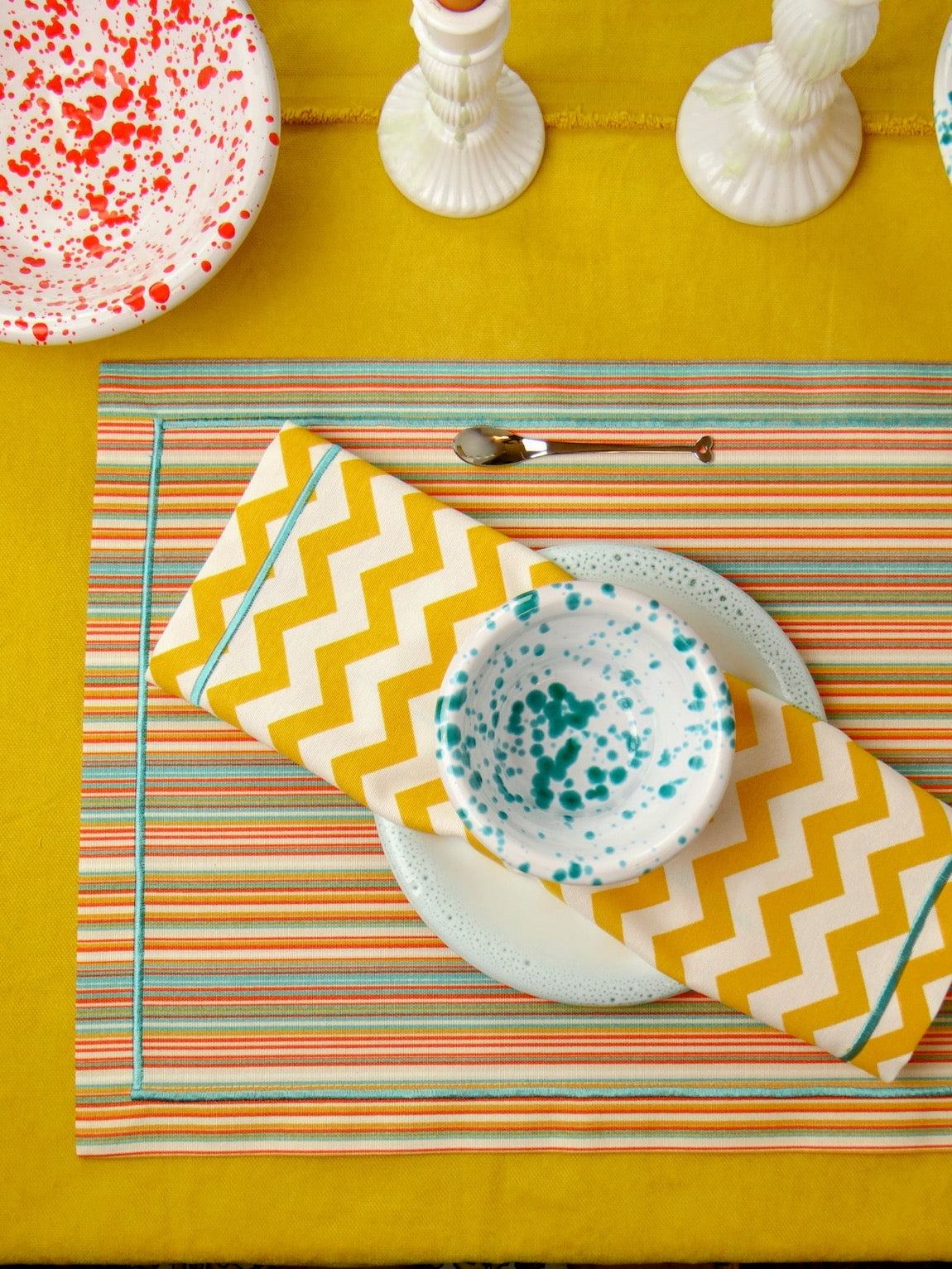 Colorful table setting with striped placemat, zigzag napkin, and patterned plates on a yellow tablecloth.