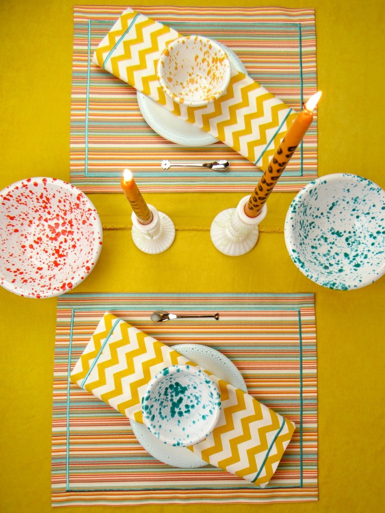 Colorful table setting with zigzag placemats, patterned plates, and candles on a yellow background.