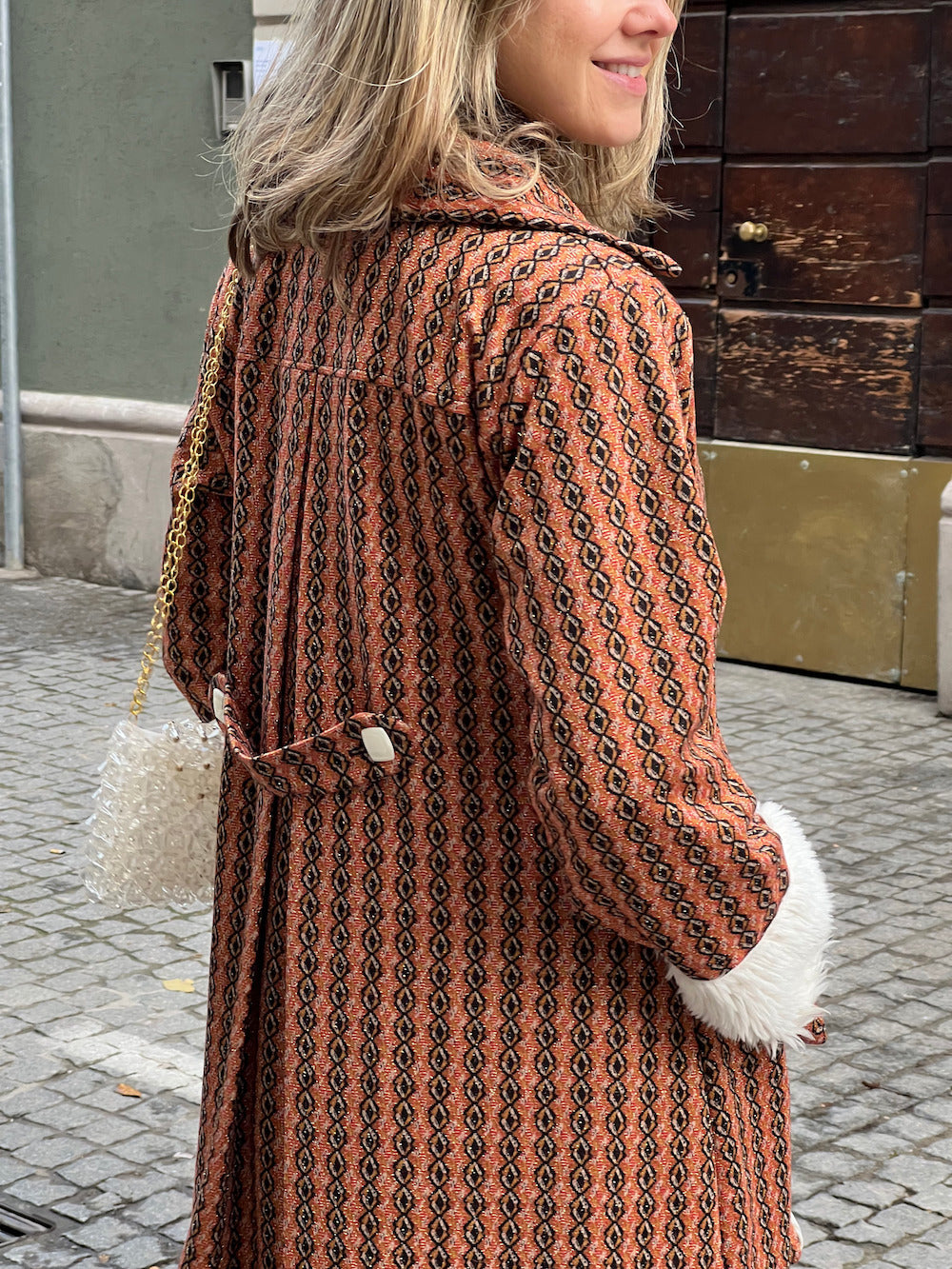 Back view of handmade burnt-orange vintage-inspired coat with geometric pattern and buckle-belt detail.