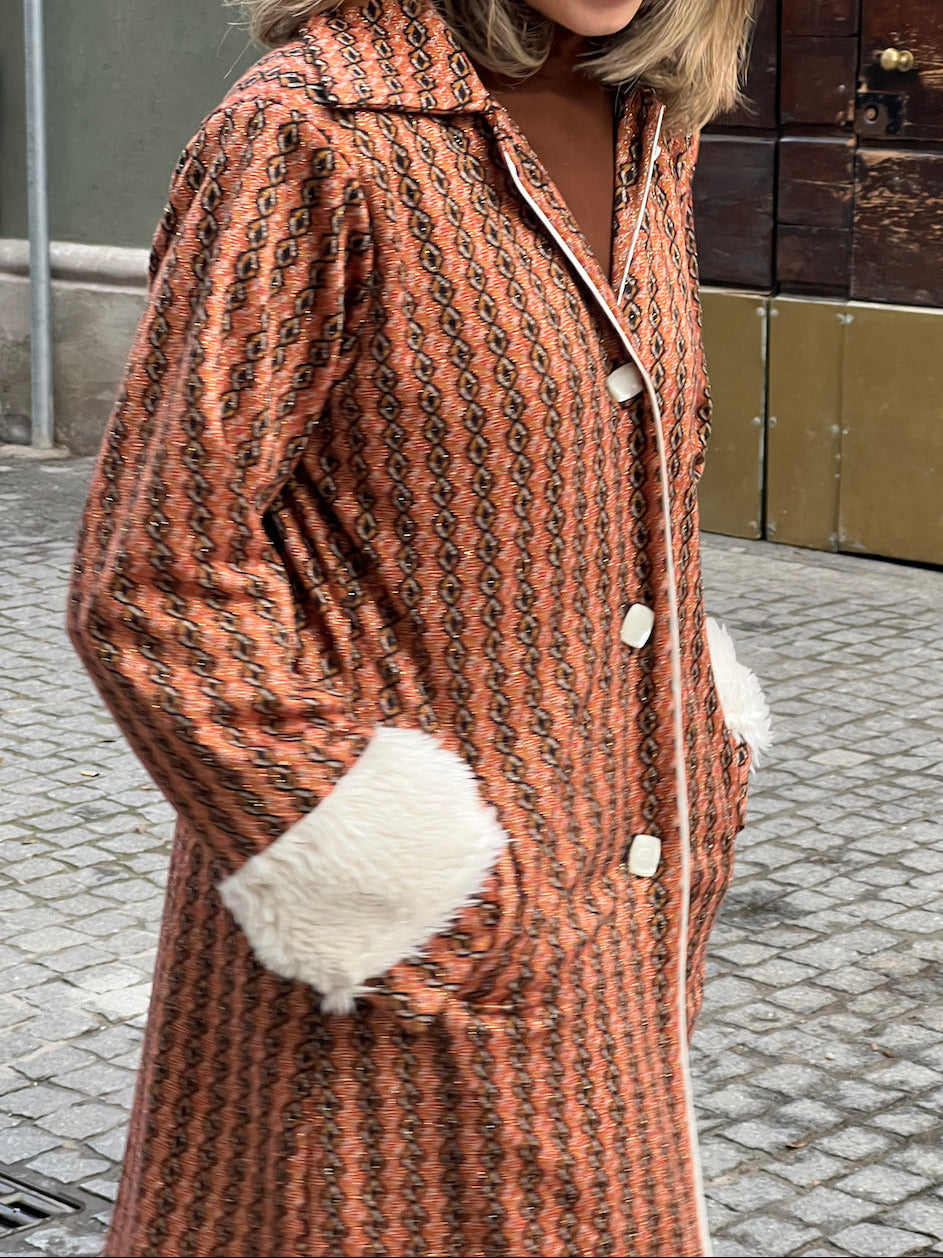 Front view of handmade burnt-orange vintage-inspired coat with geometric pattern, white faux-fur cuffs, and button closures.