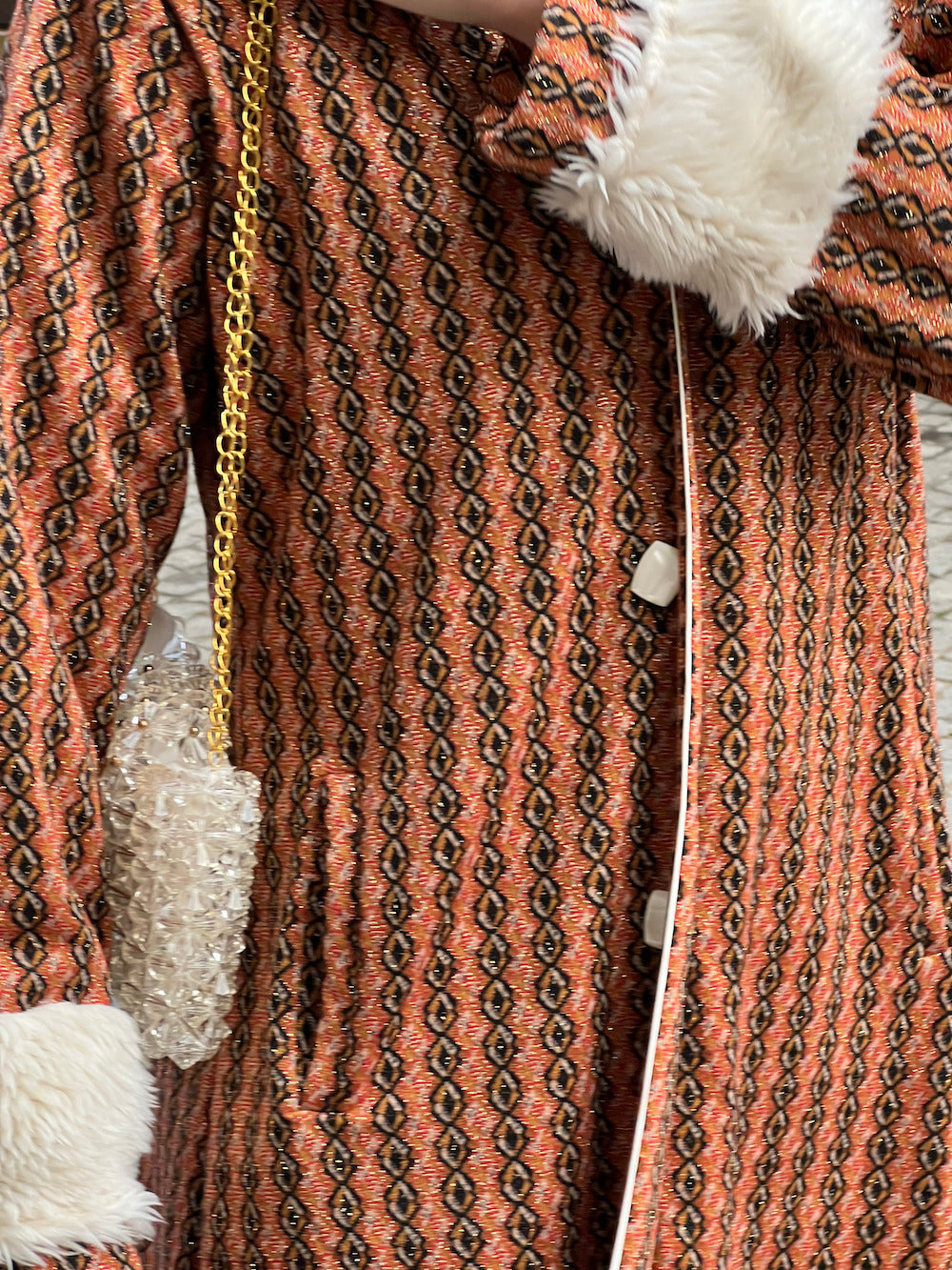 Alternate close-up of burnt-orange geometric coat highlighting fabric texture, faux-fur cuff detail and white button closures.