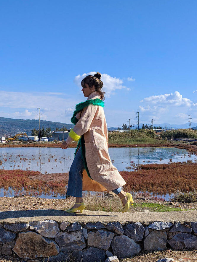 Side view of woman wearing handmade pink kimono jacket with green faux-fur collar trim and neon cuffs outdoors.